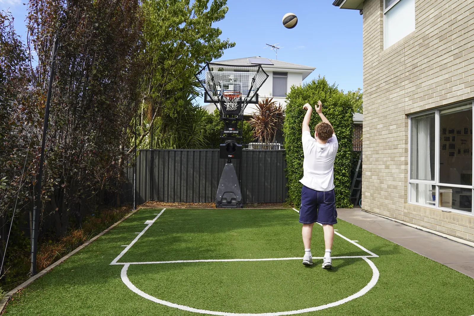 Junior player shooting on a backyard court with the TMG Assist returning the ball